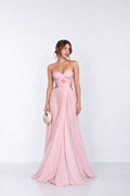 A woman modeling a strapless pink floor-length gown with a sweetheart neckline, side cutouts, and a flowing chiffon skirt, standing against a plain light gray studio background.