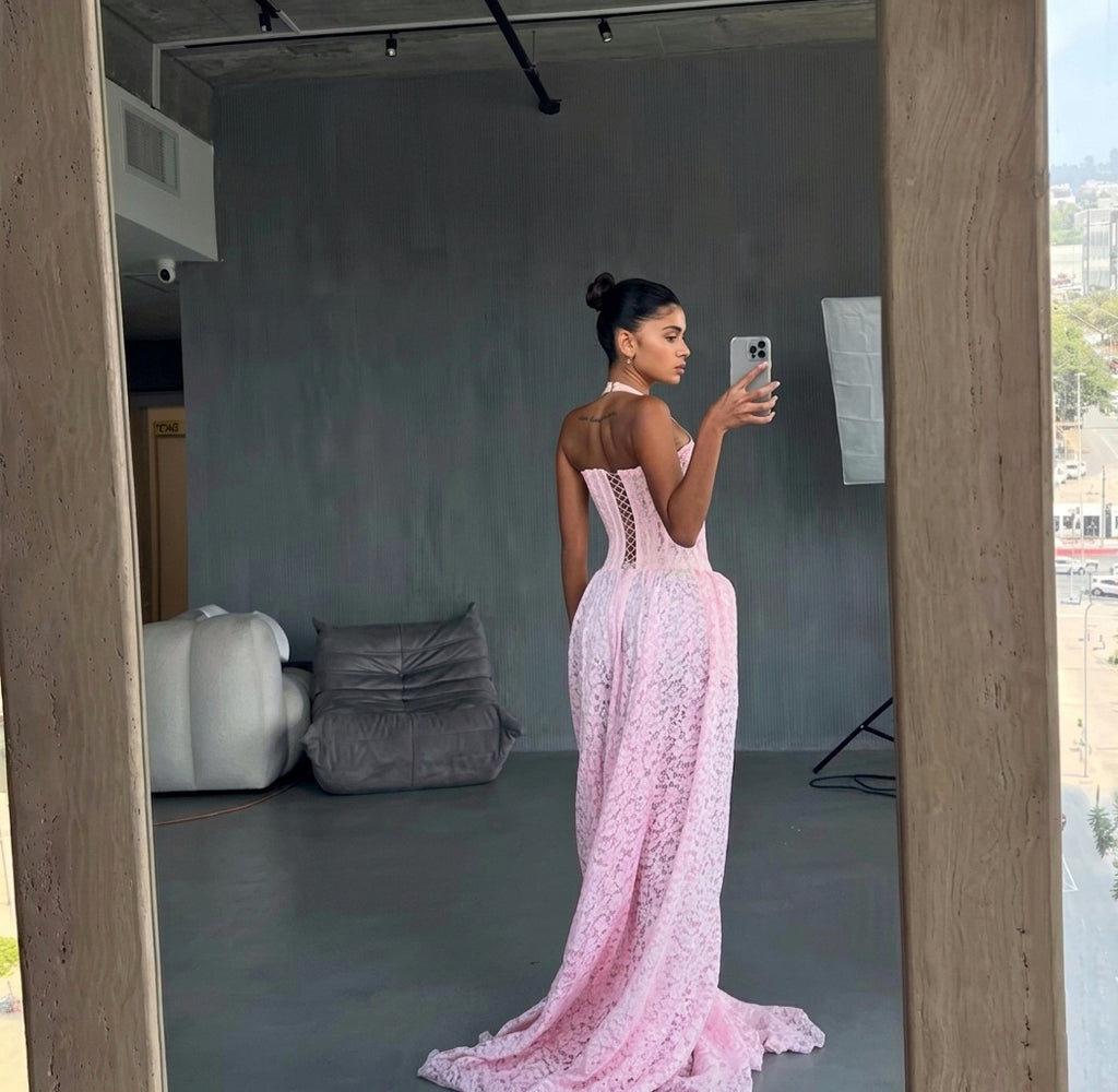 Woman in a pink lace dress taking a mirror selfie in an indoor setting.