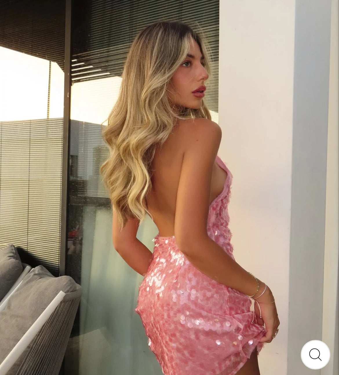 Woman in a pink sequin dress standing indoors with a blurred background