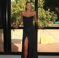 Woman in a black strapless gown with a high slit standing indoors with large windows.