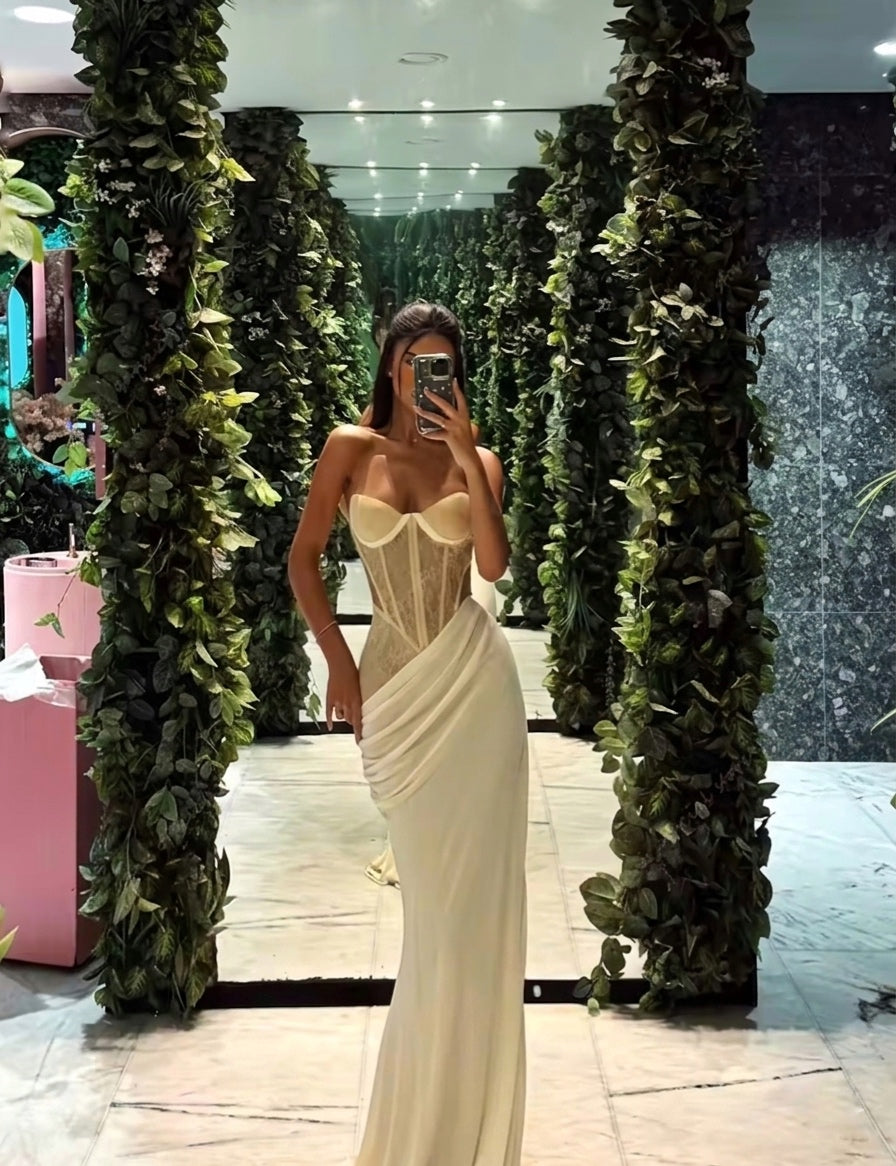 Woman in a white strapless gown standing in front of green leafy arches.