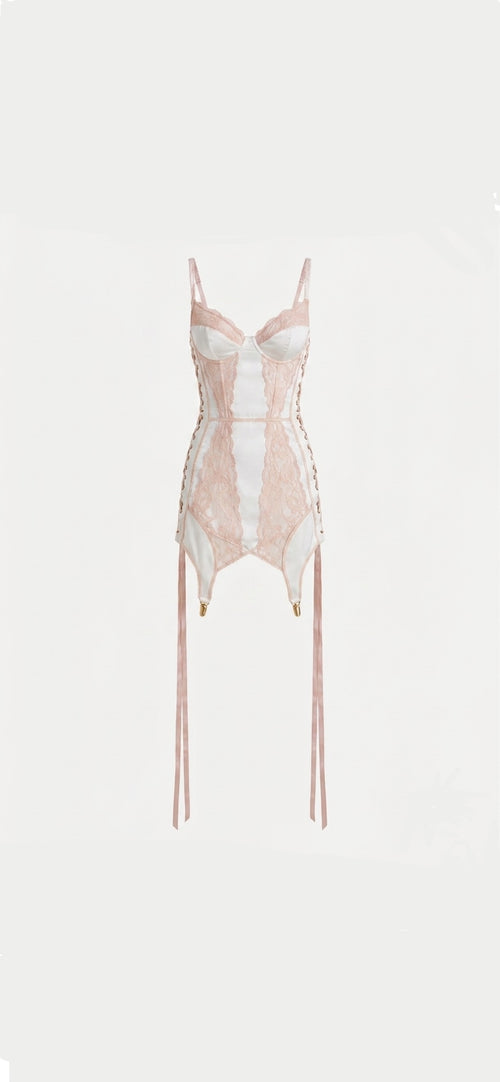 A pale pink and white lace corset bodysuit with thin shoulder straps, side lacing, and long dangling ties, shown against a plain light background.