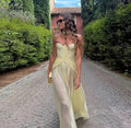Woman in a light yellow dress standing on a cobblestone path with greenery around.