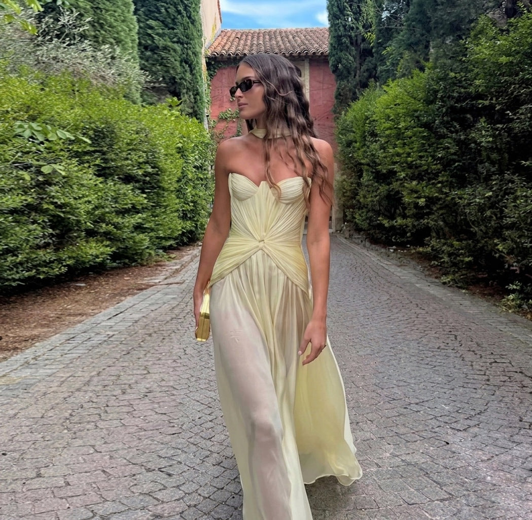 Woman in a light yellow dress standing on a cobblestone path with greenery around.