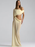 A woman modeling a floor-length, off-the-shoulder cream or pale yellow chiffon gown with a cutout at the waist, photographed against a neutral light gray studio background.
