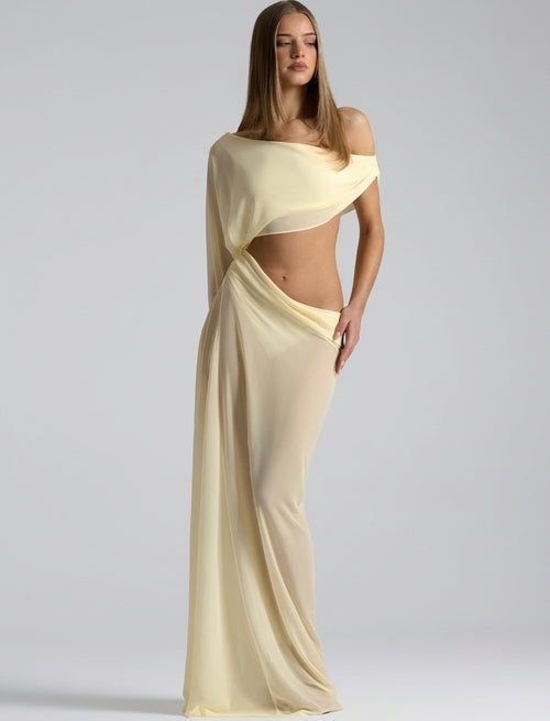 A woman modeling a floor-length, off-the-shoulder cream or pale yellow chiffon gown with a cutout at the waist, photographed against a neutral light gray studio background.
