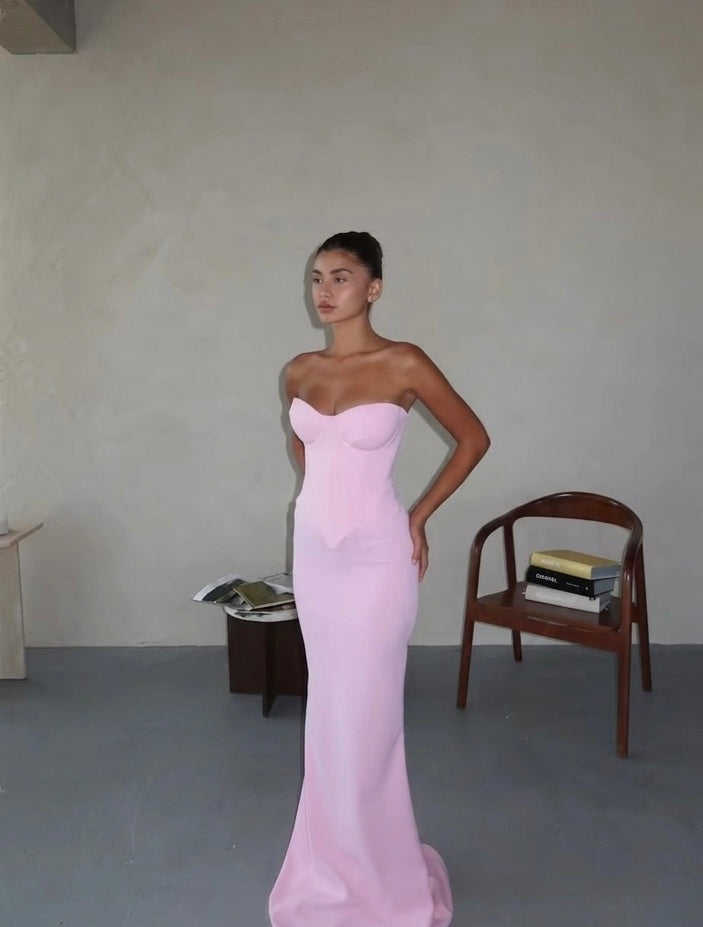 Woman in a pink strapless gown standing in a minimalistic room with a chair and table.