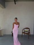 Woman in a pink strapless dress standing in a minimalistic room with a chair and table.
