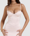 Woman wearing a light pink slip dress against a plain background